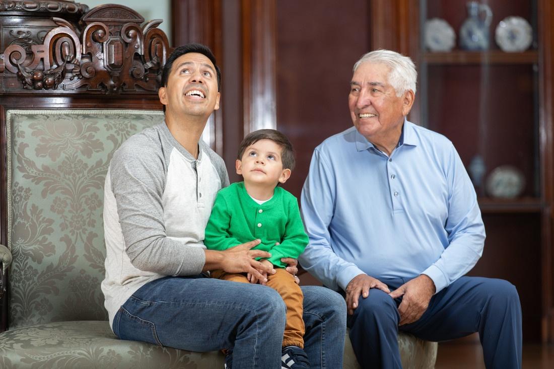A photo of a grandfather, father, and child sitting in the Crocker's historic ballroom.