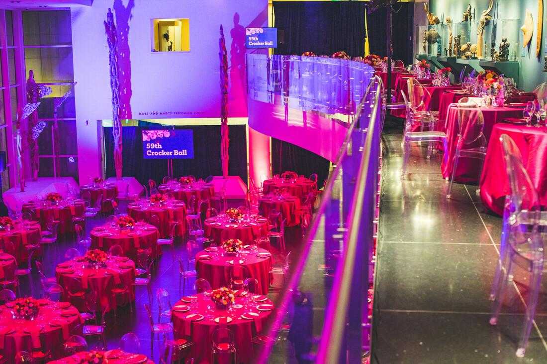 A photo of the Crocker's Friedman Court and second floor balcony, all decked out for the 59th Crocker Ball. The table clothes are pink and a purple light floods Friedman Court.