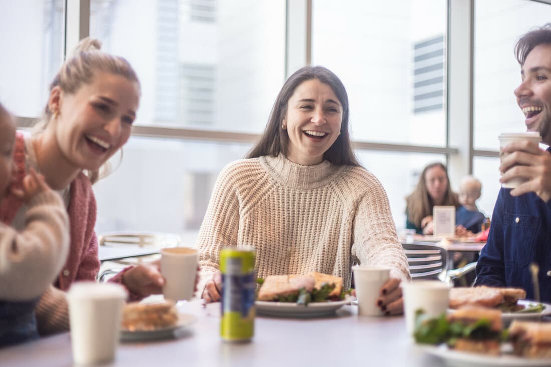 Three adults and a toddler are sitting around a cafe table in Friedman Court, enjoying lunch from the Café and each other's company. 