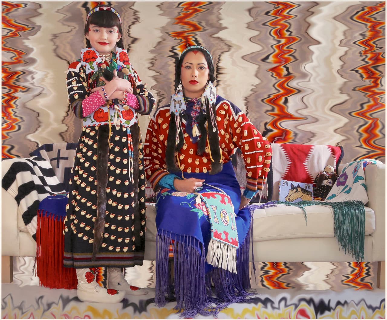 A photograph of of a woman and young girl, both dressed in traditional Native American garb. 