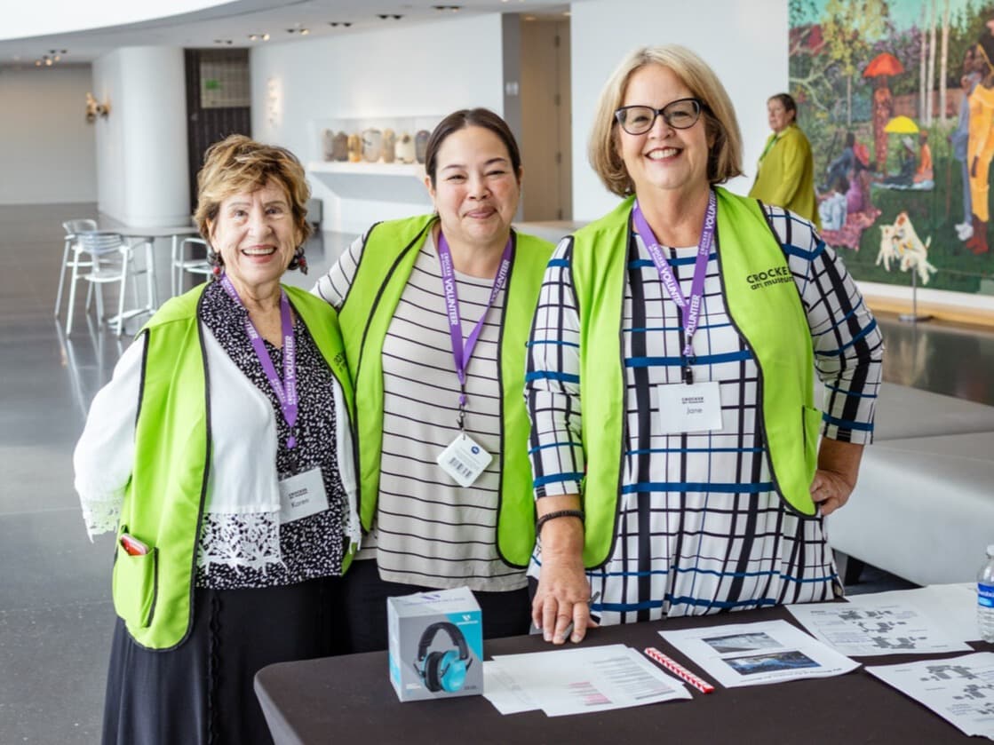 Three smiling individuals wearing bright green volunteer vests gathered at an event registration table.